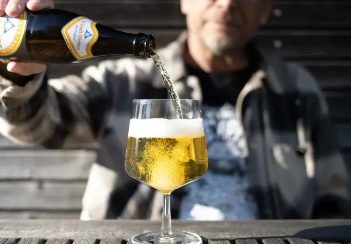Mann schenkt helles Bier ein. Die Schaumkrone ist üppig. Wer auf Bier Kalorien achtet, wählt oft ein helles Weizen.