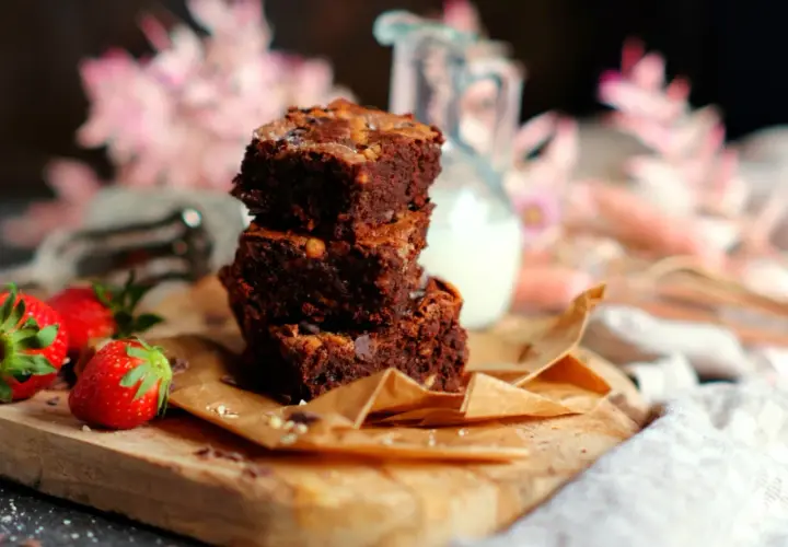Gestapelte Brownies auf einem Holzbrett, daneben Erdbeeren. Ein tolles brownie rezept ohne schokolade für Naschkatzen.