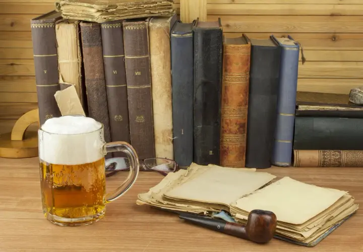 Ein Glas **Saison Bier** steht neben alten Büchern und einer Pfeife.