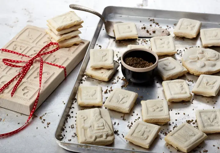 Holzmodel für Springerle backen, daneben frisch gebackene Kekse mit verschiedenen Motiven auf einem Blech.