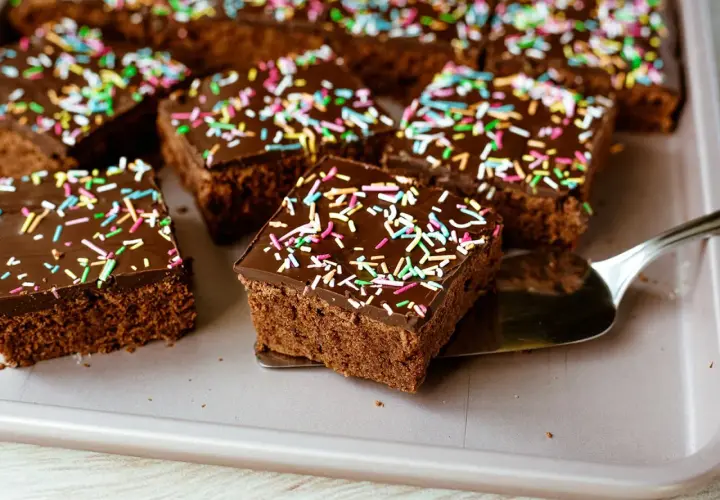 Saftiger schokokuchen blech mit bunten Streuseln, bereit zum Servieren. Ein Stück wird gerade mit einem Tortenheber herausgenommen.