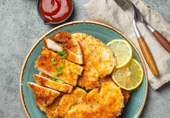 Knusprige Schnitzel mit Treber Panade, garniert mit Zitrone und Schnittlauch, daneben eine Schale Ketchup.