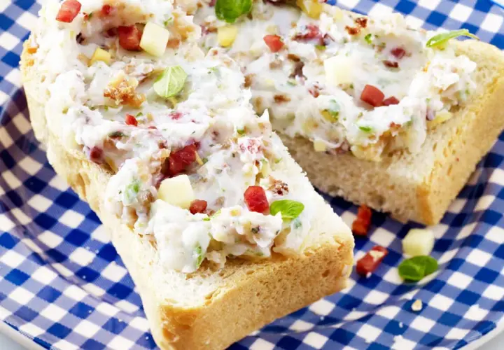 Schmalz-Brotaufstriche mit Speck und Kräutern auf rustikalem Brot, serviert auf blau-weiß karierter Platte.