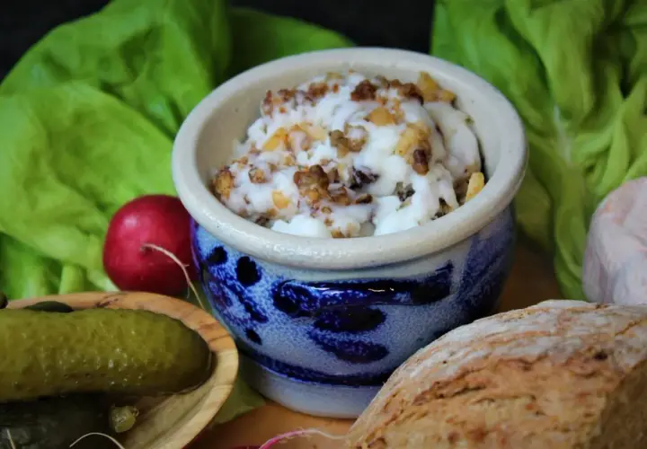 Griebenschmalz, ein traditionelles Gericht, in einem blauen Steingut-Napf, serviert mit Brot, Radieschen und Gewürzgurken.