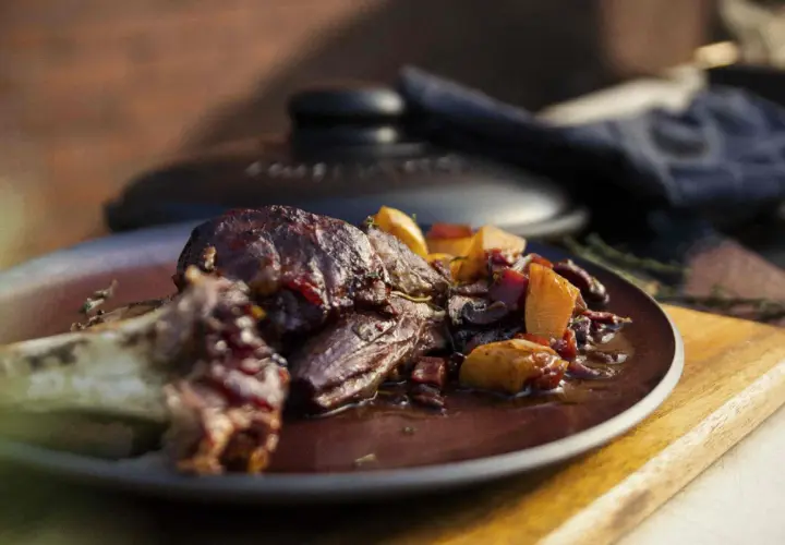 Ein saftiges Lammhaxe Rezept, serviert mit Wurzelgemüse in einer dunklen Sauce auf einem Teller.
