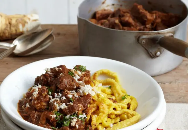 Herzhaftes Gulasch mit Spätzle, das Fleisch wurde perfekt mariniert. Daneben ein Meerrettich und Besteck.