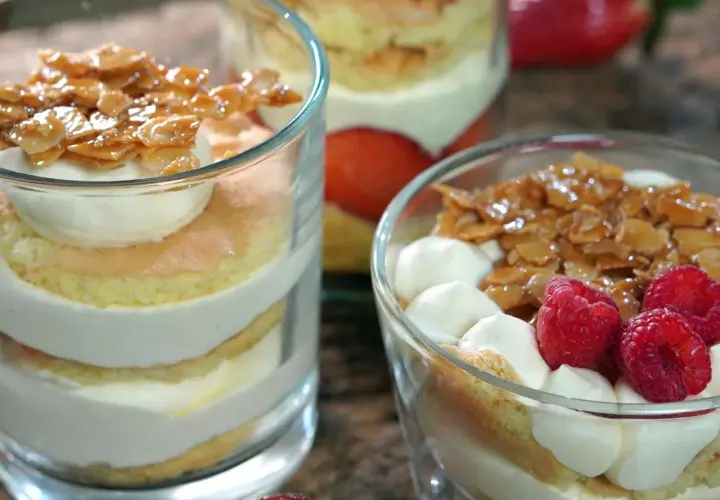 Schichten von Biskuit, Sahne und karamellisierten Mandeln, garniert mit Beeren. Ein köstlicher Bienenstich im Glas.