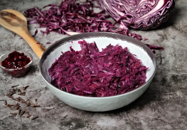 Schon probiert? Dieses rotkohl rezept einfach ist ein Genuss! Serviert in einer Schüssel, daneben ein Löffel, Gewürznelken und Preiselbeeren.