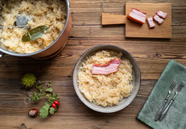 Herzhaftes Sauerkraut mit Speck, perfekt für ein Oktoberfest-Rezept. Ein Topf mit Sauerkraut und ein Teller mit dem fertigen Gericht stehen bereit.