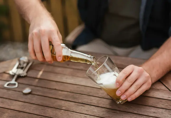 Mann schenkt Bier ein. Vielleicht für ein 20-Liter-Bier-Rezept? Ein Kronkorken und ein Flaschenöffner liegen bereit.