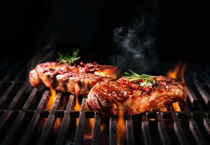 Zwei saftige Steaks brutzeln auf dem Grill, verfeinert mit einer Schwarzbier-Marinade, Rosmarin und rosa Pfeffer.