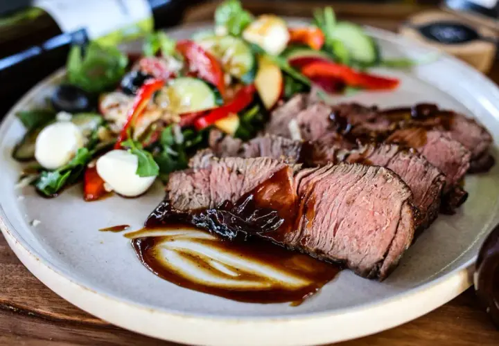 Saftiges Roastbeef als Beilage mit einem frischen Salat aus Tomaten, Gurken, Paprika und Mozzarella-Kugeln, beträufelt mit dunkler Sauce.