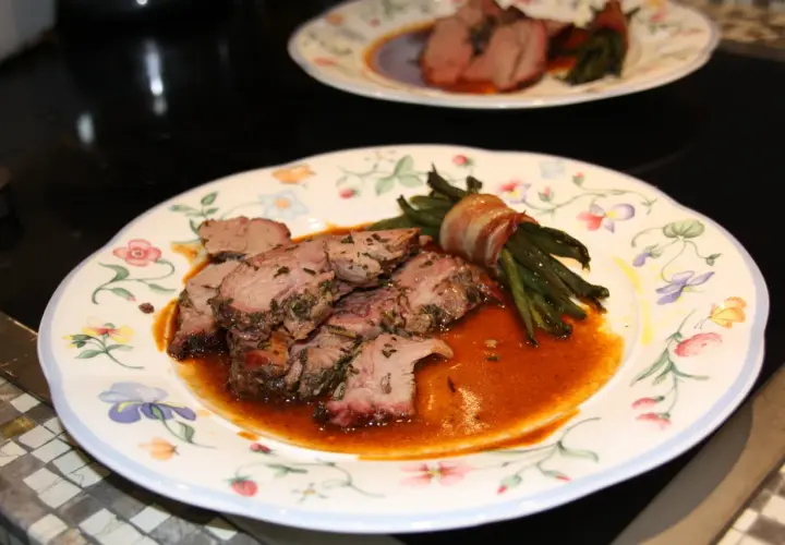Zarte Lammfleischscheiben mit Kräutern, serviert mit Speck-umwickelten grünen Bohnen und einer köstlichen Sauce zu Lamm.