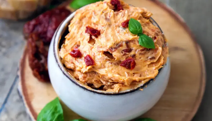 Cremige Tomatenbutter selbst machen: Ein Schälchen mit köstlicher Tomatenbutter, garniert mit Basilikum und getrockneten Tomatenstücken.