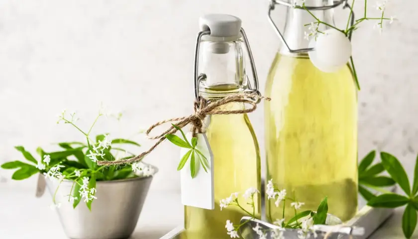 Zwei Flaschen mit omas waldmeistersirup, verziert mit frischen Waldmeisterzweigen und kleinen weißen Blüten.