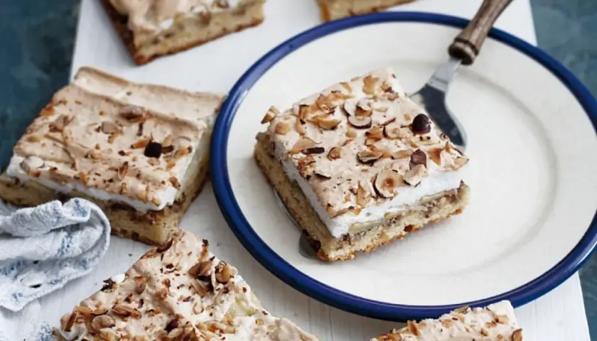 Saftiger Apfelkuchen mit Boskop-Äpfeln und Baiserhaube, bestreut mit gehackten Nüssen. Ein Stück auf einem Teller, bereit zum Genuss.