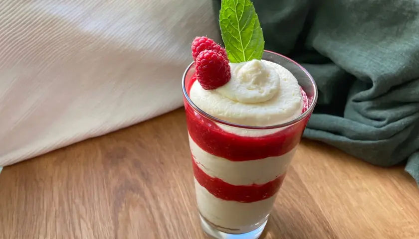 Schichtdessert im Glas mit Himbeersoße und einfacher Schmandcreme, garniert mit frischen Himbeeren und Minze.