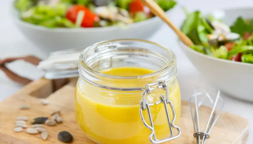 Frische, selbstgemachte Salatsauce im Glas, bereit für den Salat. Mit Kernen und einem kleinen Schneebesen daneben.