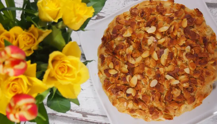 Ein köstlicher bienenstich ohne sahne, bedeckt mit gerösteten Mandelblättchen, neben einem Strauß gelber Rosen.