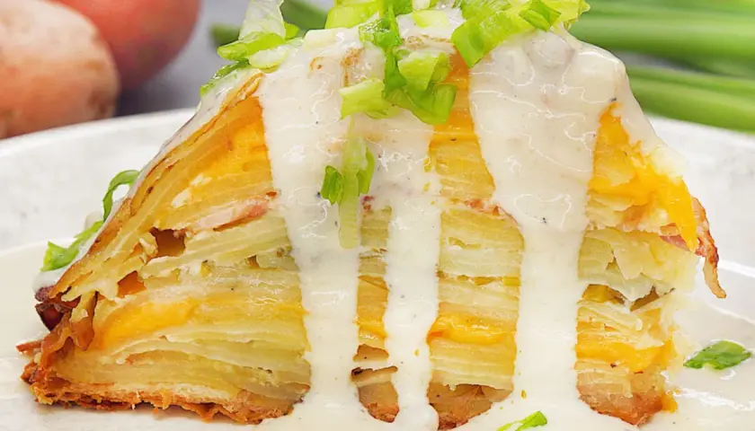 Ein Stück Kartoffelkuchen nach altem Rezept, geschichtet mit Käse und überzogen mit cremiger Sauce und Frühlingszwiebeln.
