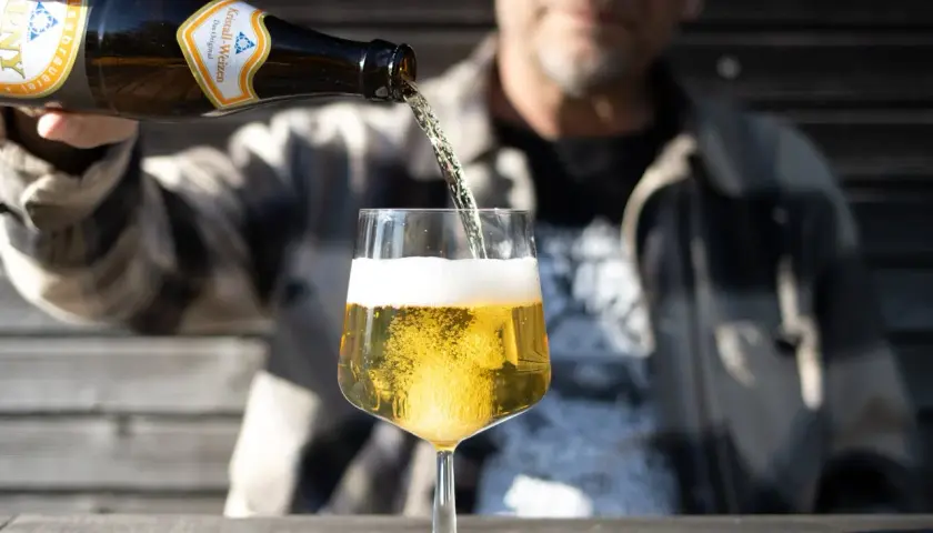 Mann schenkt helles Bier ein. Die Schaumkrone ist üppig. Wer auf Bier Kalorien achtet, wählt oft ein helles Weizen.