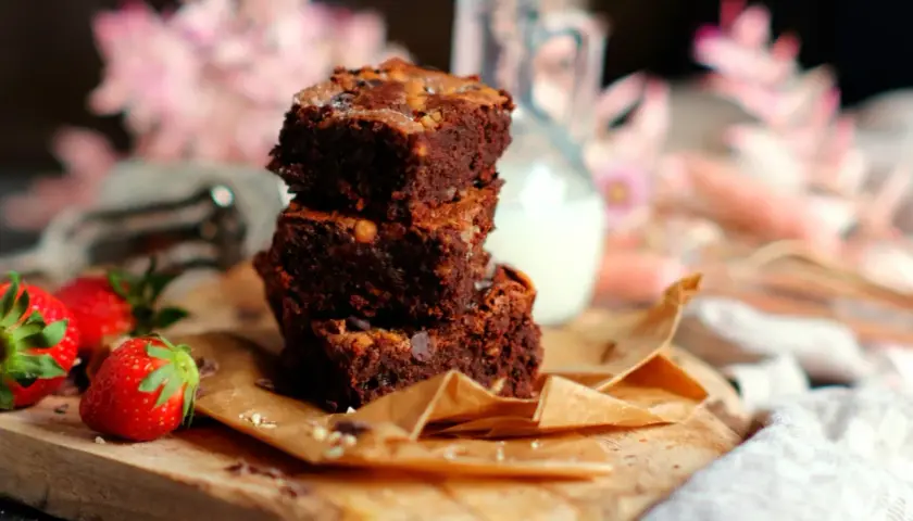 Gestapelte Brownies auf einem Holzbrett, daneben Erdbeeren. Ein tolles brownie rezept ohne schokolade für Naschkatzen.