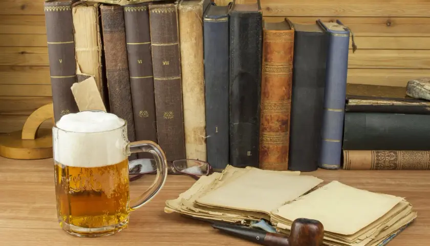 Ein Glas **Saison Bier** steht neben alten Büchern und einer Pfeife.