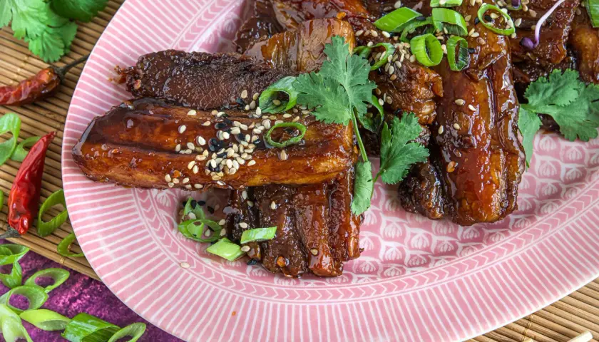 Glasierter schweinebauch asiatisch, garniert mit Frühlingszwiebeln und Sesam. Rote Chilischoten und Koriander runden das Gericht ab.