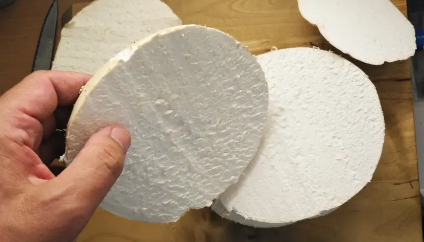 Ein Mensch hält eine dicke Scheibe eines riesigen Bovists, bereit für ein leckeres riesenbovist rezept. Mehrere weitere Scheiben liegen auf einem Holzbrett.
