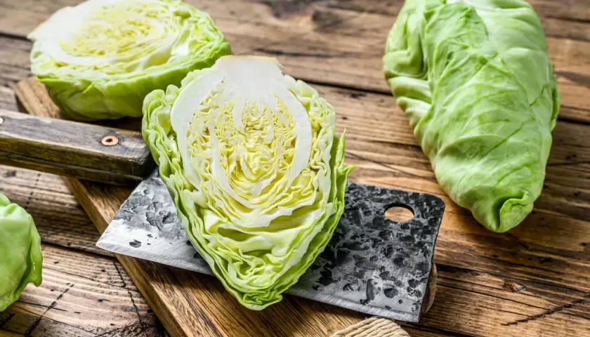 Frischer spitzkohl roh, halbiert und auf einem Holzbrett mit einem Hackmesser. Bereit für die Zubereitung eines knackigen Salats.
