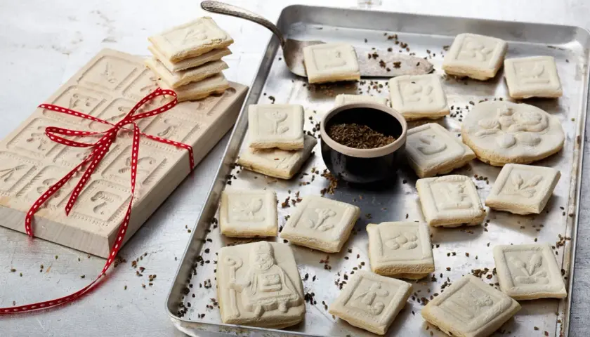 Holzmodel für Springerle backen, daneben frisch gebackene Kekse mit verschiedenen Motiven auf einem Blech.