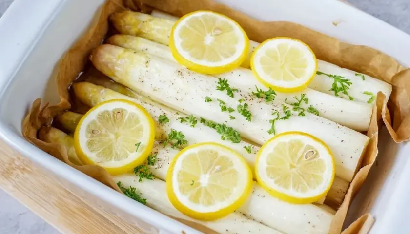 Zubereitung gefrorener Spargel im Backofen: Weißer Spargel mit Zitronenscheiben und Petersilie in einer Auflaufform.