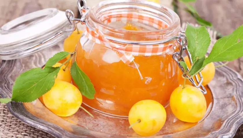 Ein Glas mit leuchtend orangefarbener Mirabellenmarmelade, umgeben von frischen Früchten und Blättern. Ein schönes Bild für ein Mirabellenmarmelade Rezept.