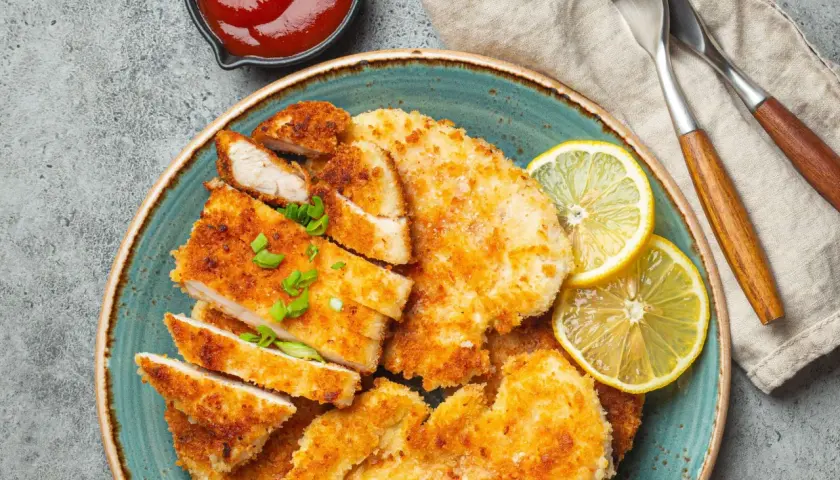 Knusprige Schnitzel mit Treber Panade, garniert mit Zitrone und Schnittlauch, daneben eine Schale Ketchup.