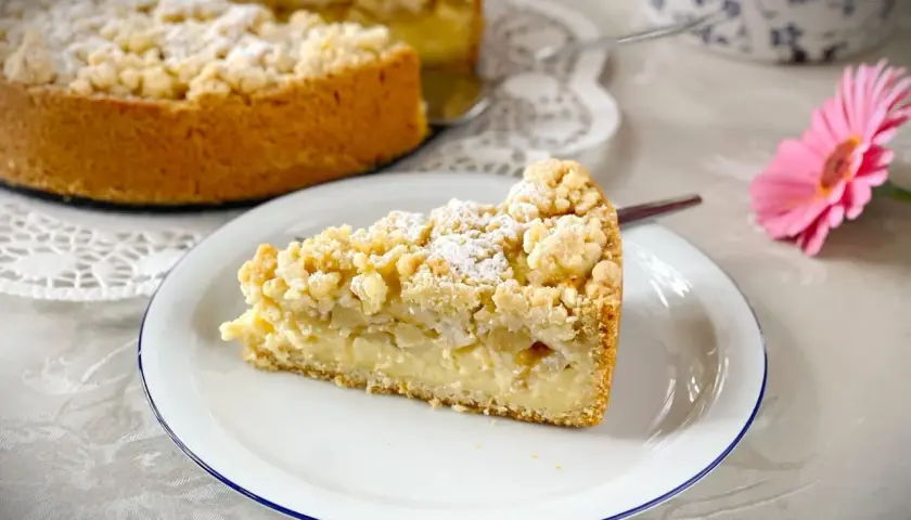 Ein Stück saftiger versunkener Apfelkuchen mit Pudding und Streuseln, bestäubt mit Puderzucker.