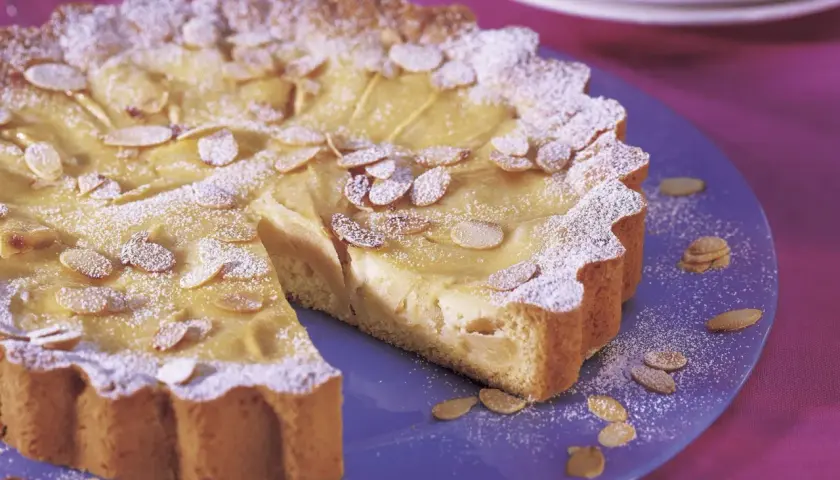 Ein köstlicher Apfelkuchen mit Guss, bestreut mit Puderzucker und Mandelblättchen, auf einem blauen Teller.