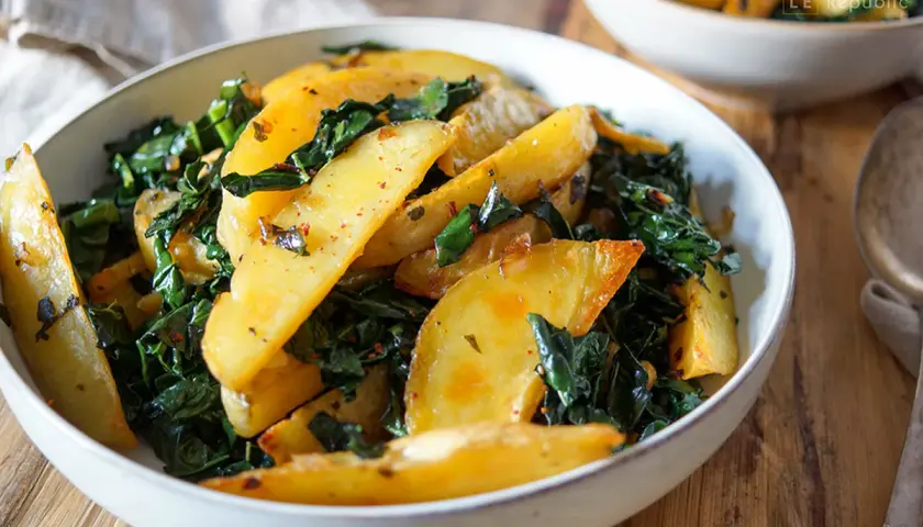 Schwarzkohl-Rezept: goldbraune Kartoffelspalten mit gedünstetem Schwarzkohl, gewürzt mit Chili und Kräutern, serviert in einer Schüssel.