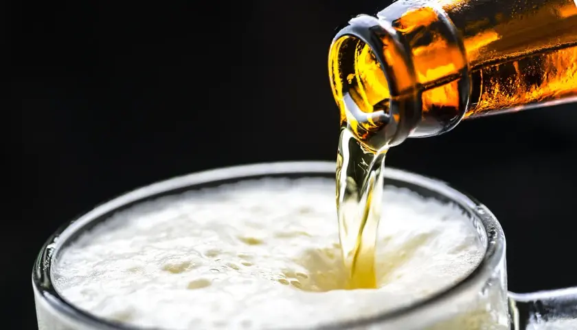 Ein bernsteinfarbenes alkoholfreies Bier fließt aus einer Flasche in ein Glas mit viel Schaum. Perfekt für alle, die alkoholfreies Bier selber brauen möchten.