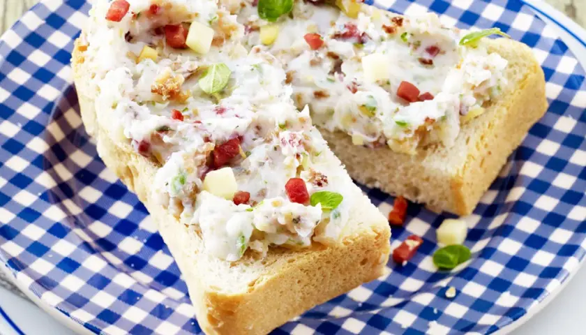 Schmalz-Brotaufstriche mit Speck und Kräutern auf rustikalem Brot, serviert auf blau-weiß karierter Platte.