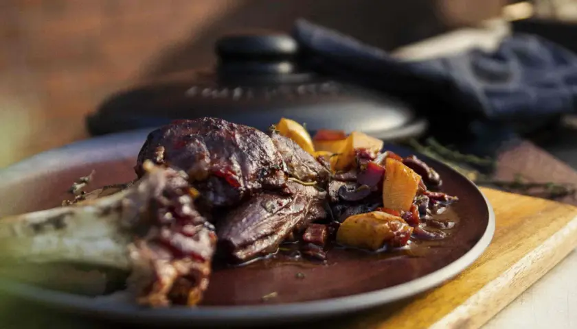 Ein saftiges Lammhaxe Rezept, serviert mit Wurzelgemüse in einer dunklen Sauce auf einem Teller.