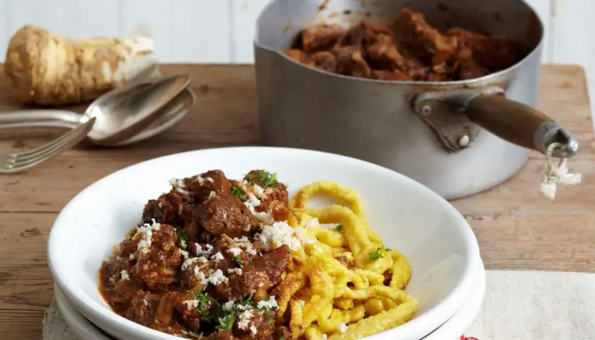 Herzhaftes Gulasch mit Spätzle, das Fleisch wurde perfekt mariniert. Daneben ein Meerrettich und Besteck.