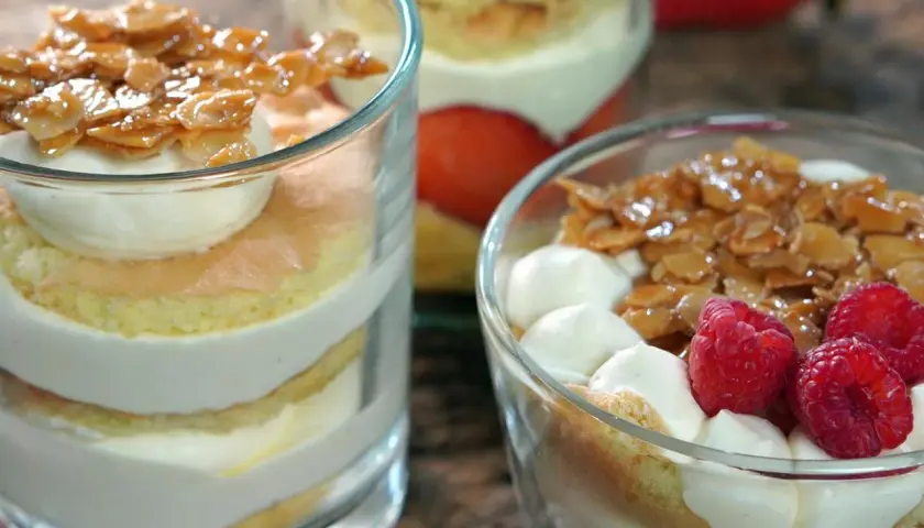 Schichten von Biskuit, Sahne und karamellisierten Mandeln, garniert mit Beeren. Ein köstlicher Bienenstich im Glas.