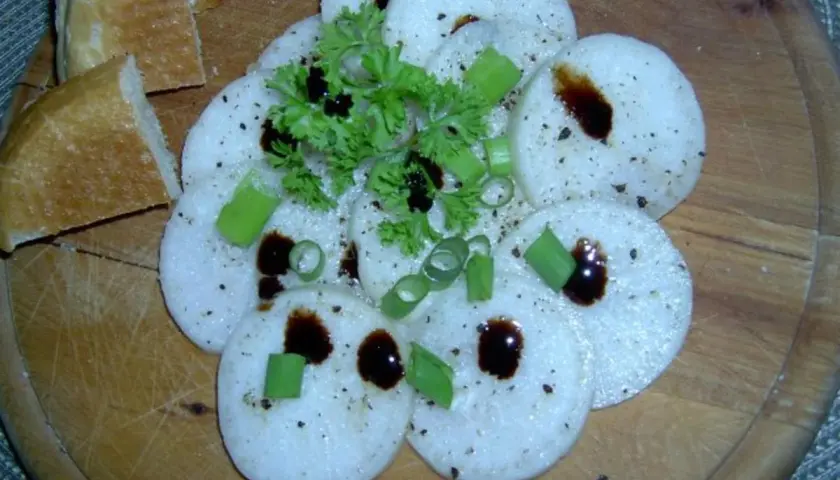 Frisch geschnittener Radi mit Kräutern und dunklem Balsamico auf Holzbrett, dazu Baguette.