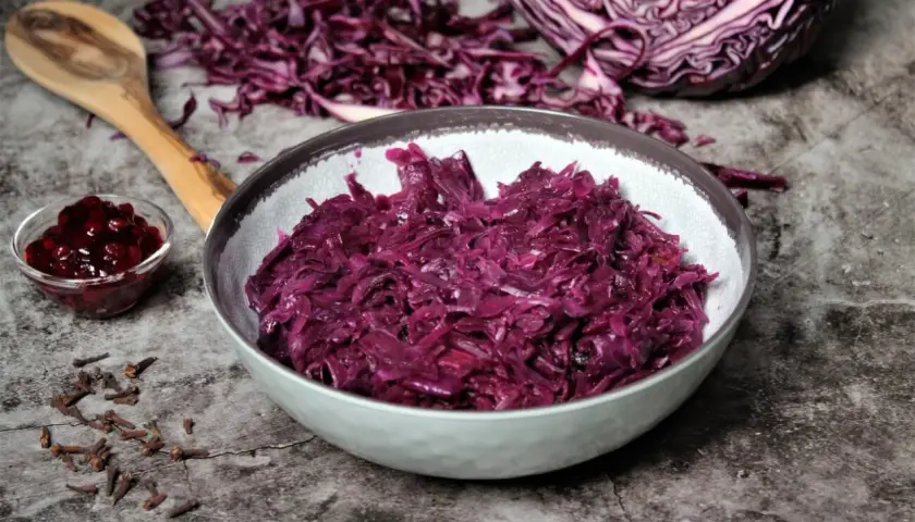 Schon probiert? Dieses rotkohl rezept einfach ist ein Genuss! Serviert in einer Schüssel, daneben ein Löffel, Gewürznelken und Preiselbeeren.