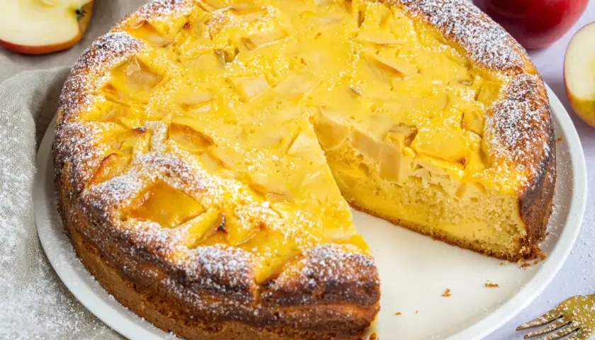 Ein schneller, saftiger Apfelkuchen mit Quark, bestäubt mit Puderzucker. Daneben liegen Äpfel und goldene Gabeln.