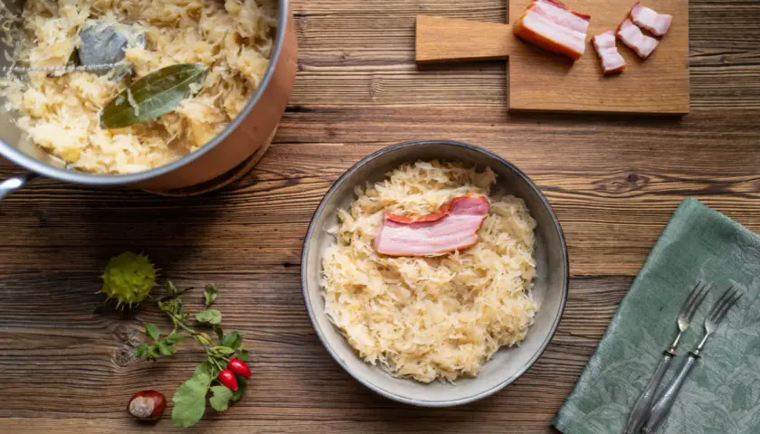 Herzhaftes Sauerkraut mit Speck, perfekt für ein Oktoberfest-Rezept. Ein Topf mit Sauerkraut und ein Teller mit dem fertigen Gericht stehen bereit.