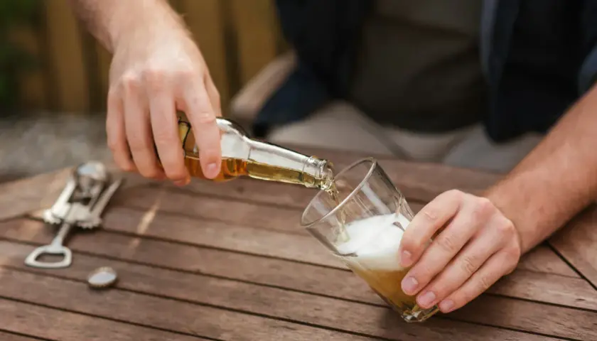 Mann schenkt Bier ein. Vielleicht für ein 20-Liter-Bier-Rezept? Ein Kronkorken und ein Flaschenöffner liegen bereit.
