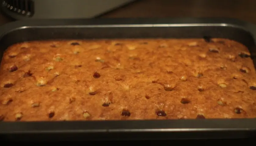 Frisch gebackener, goldbrauner tante mathildas kirschkuchen in einer rechteckigen Backform. Kleine Kirschstücke sind im Teig verteilt.