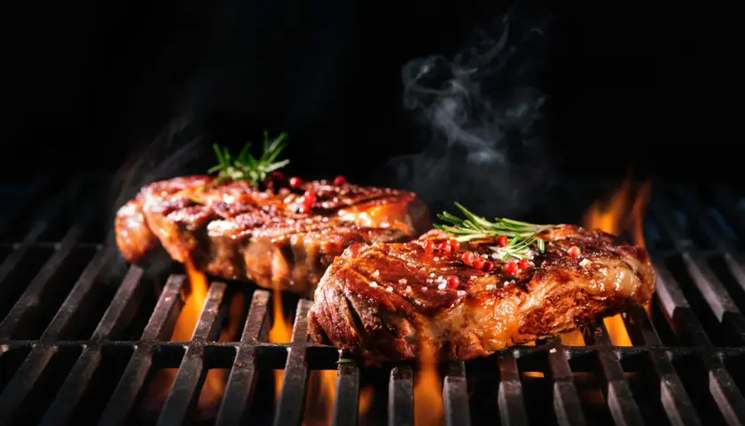 Zwei saftige Steaks brutzeln auf dem Grill, verfeinert mit einer Schwarzbier-Marinade, Rosmarin und rosa Pfeffer.
