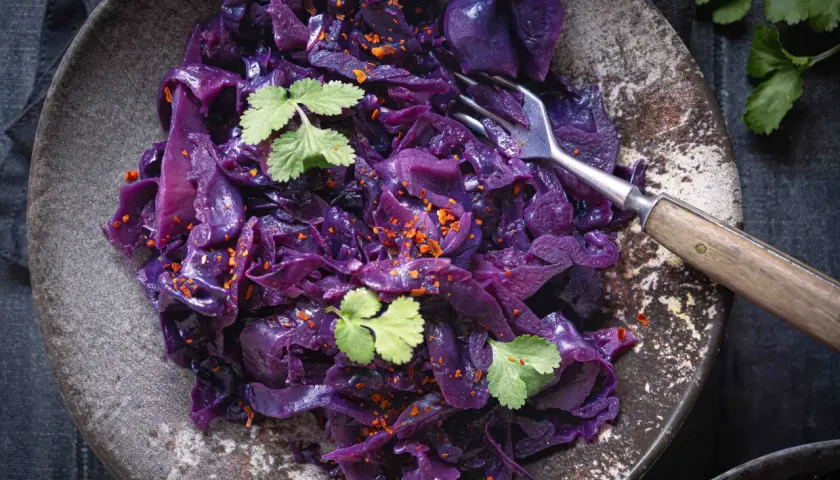 Ein Teller mit dampfendem rotkohl, verfeinert mit frischer Petersilie und Chili-Flocken. Eine Gabel ruht darin, bereit zum Genießen.